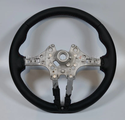 BMW F Series steering wheel upgrade with black leather and tri-color stitching on plain background