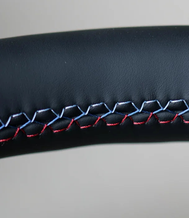 Close-up of black leather BMW F Series steering wheel with tri-color stitching detail